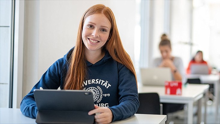 Studierende sitzt in der Bibliothek vor ihrem Tablet.