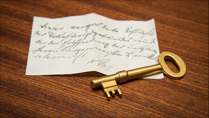Ein beschriebenes Stück Papier, auf dem ein goldener Schlüssel liegt
