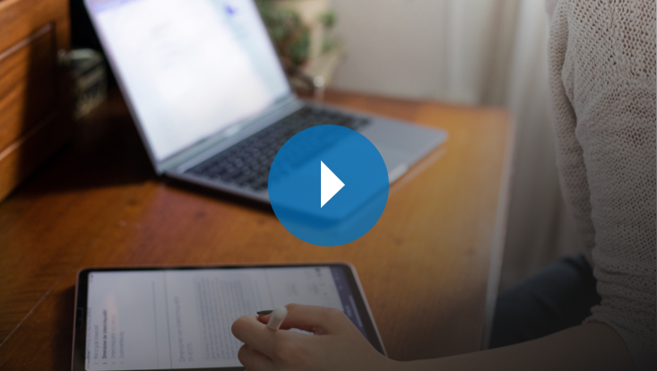 Person macht sich Notizen auf einem Tablet vor einem Laptop