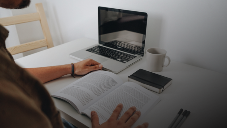 Mann ließt Buch vor Laptop